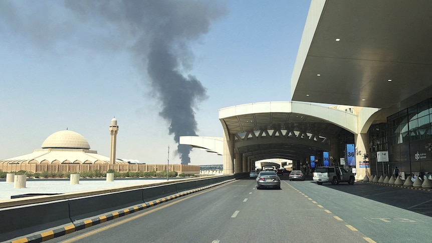 A large plume of black smoke as seen from a multi-lane road with a dome shaped building on left