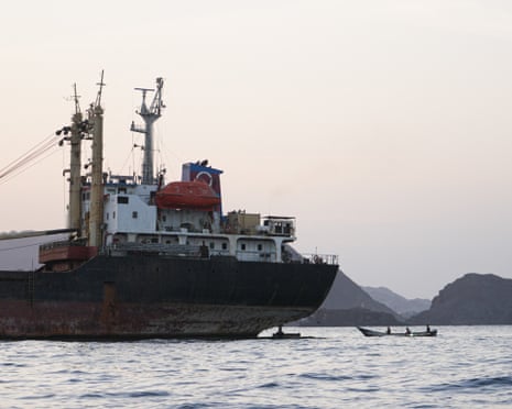 A rusty cargo ship anchored off Yemen's coast near Bab al-Mandeb, with a small boat passing