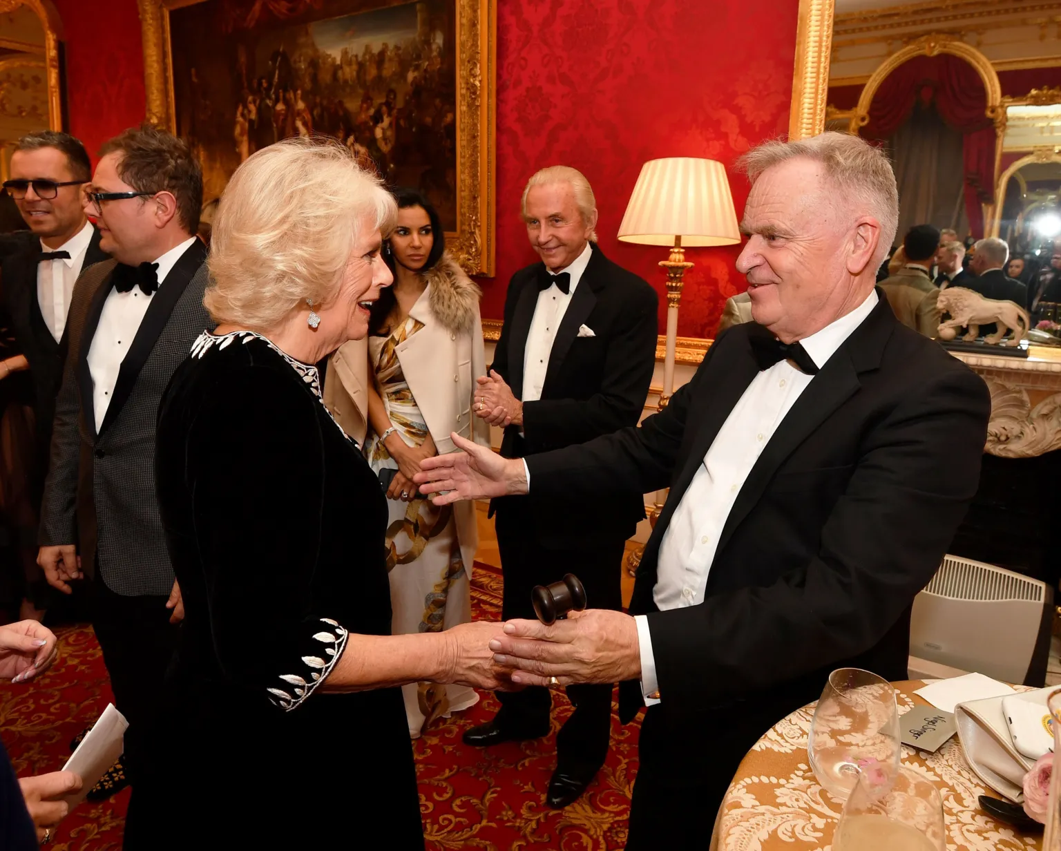 Getty Images Queen Camilla and Jeffrey Archer at a charity reception in 2018. They are greeting each other warmly and both are dressed formally.