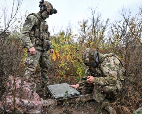 Ukrainian soldiers in camouflage set up a Starlink terminal case at a combat position outdoors.